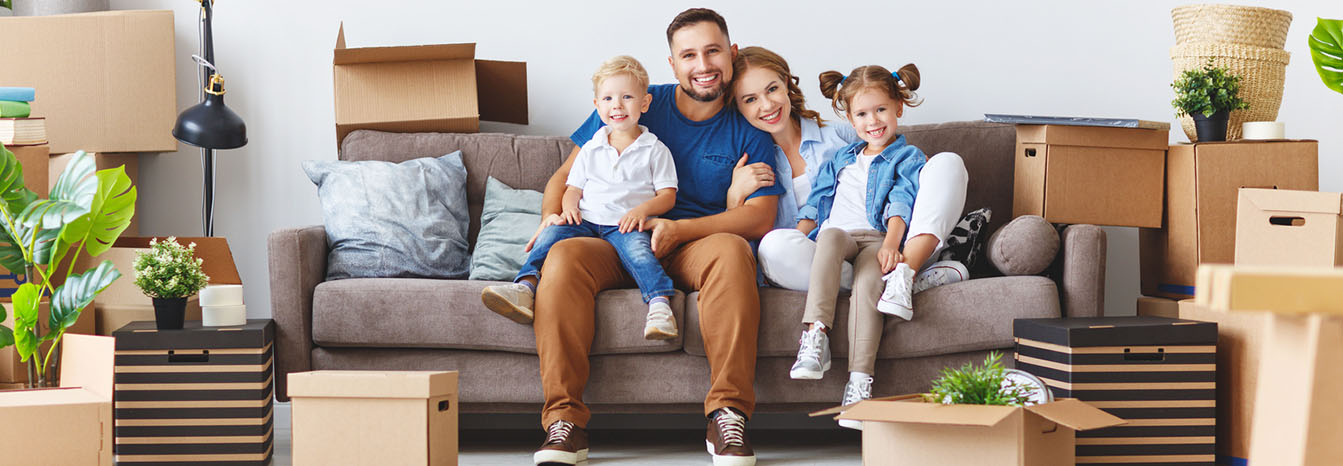 Happy couple in living room with two kids and boxes from moving